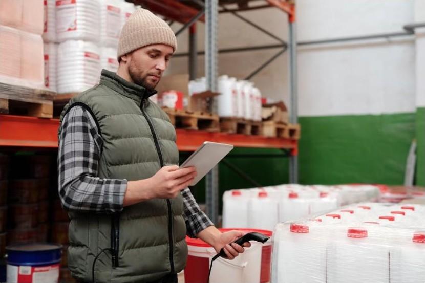 Warehouse worker checking inventory on a tablet and handheld scanner between storage racks